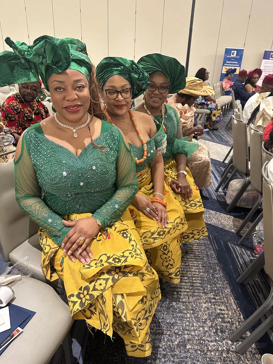 Three women in green and gold traditional attire at a Ngwa gathering.